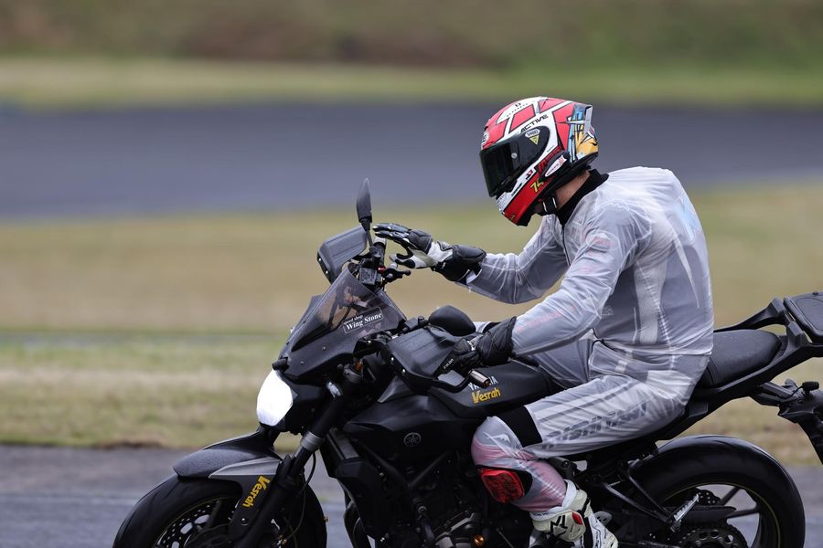 レインウェア姿のライダーがバイクにまたがり走行する様子（横から）